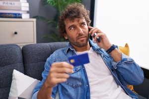 Homem a segurar o seu cartão de débito enquanto efetua um telefonema